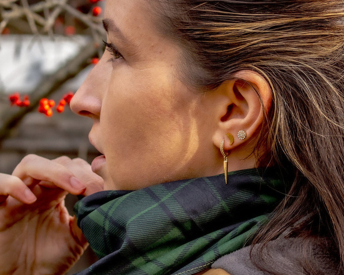 Woman wearing a freen plaid scarf with a blurred background of red berries and wooden structures