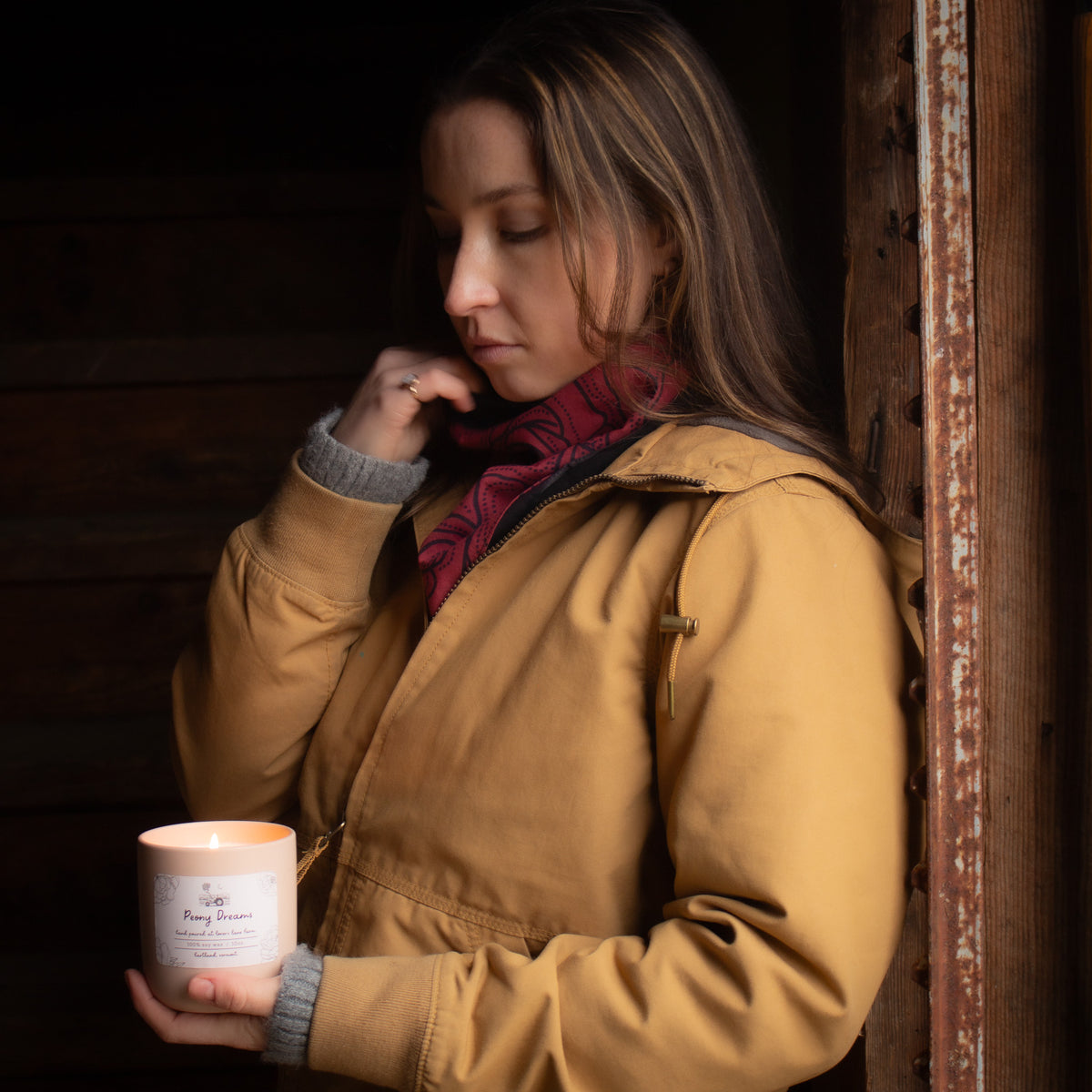 Woman in an llbean jacket and red bandana holding a candle in a dimly lit setting